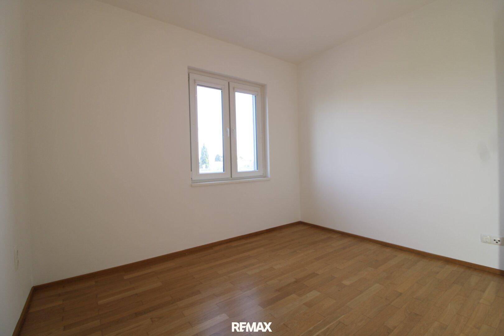 Helles Schlafzimmer mit Parkettboden und einem großen Fenster, bereit zur individuellen Gestaltung.