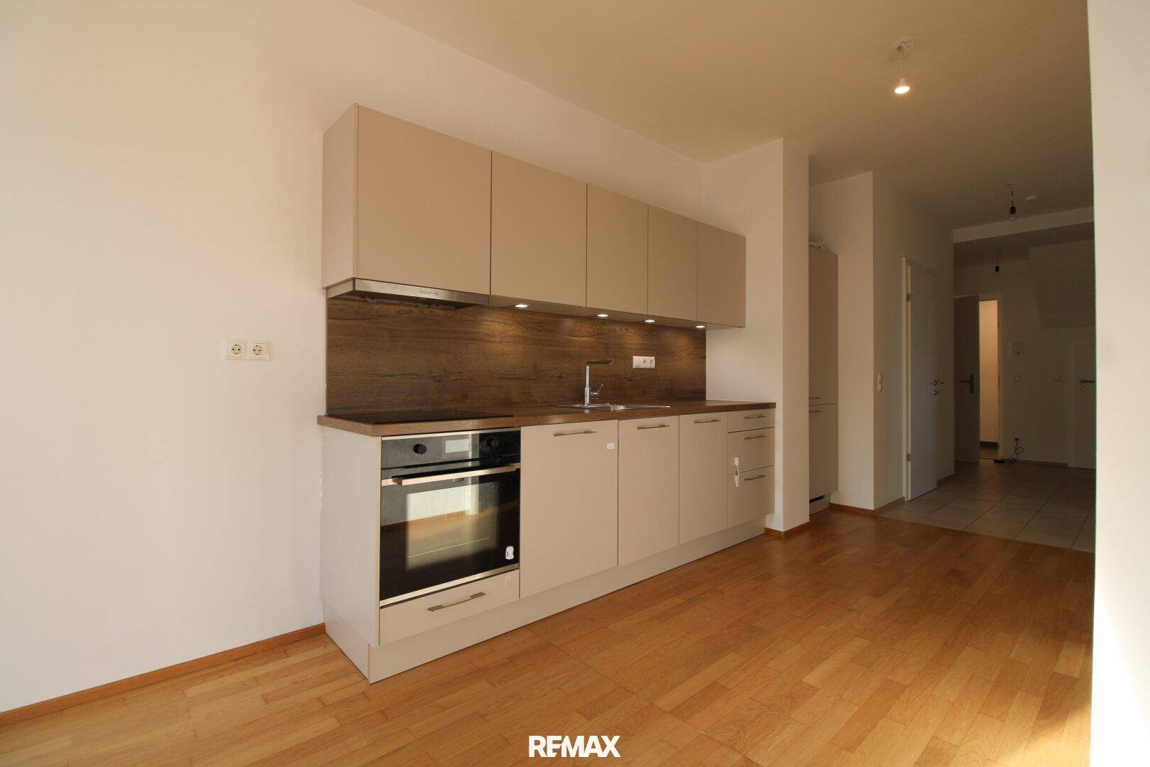 Moderne Küchenzeile mit hellen Schränken, integriertem Backofen und Holz-Arbeitsplatte.