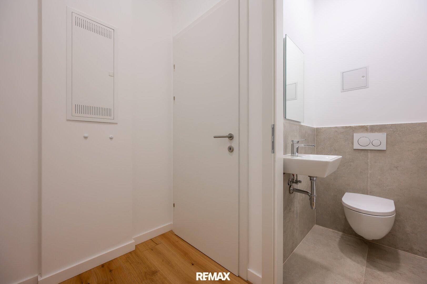 Modernes Gäste-WC mit wandhängender Toilette, kleinem Waschbecken und teilgefliesten Wänden.