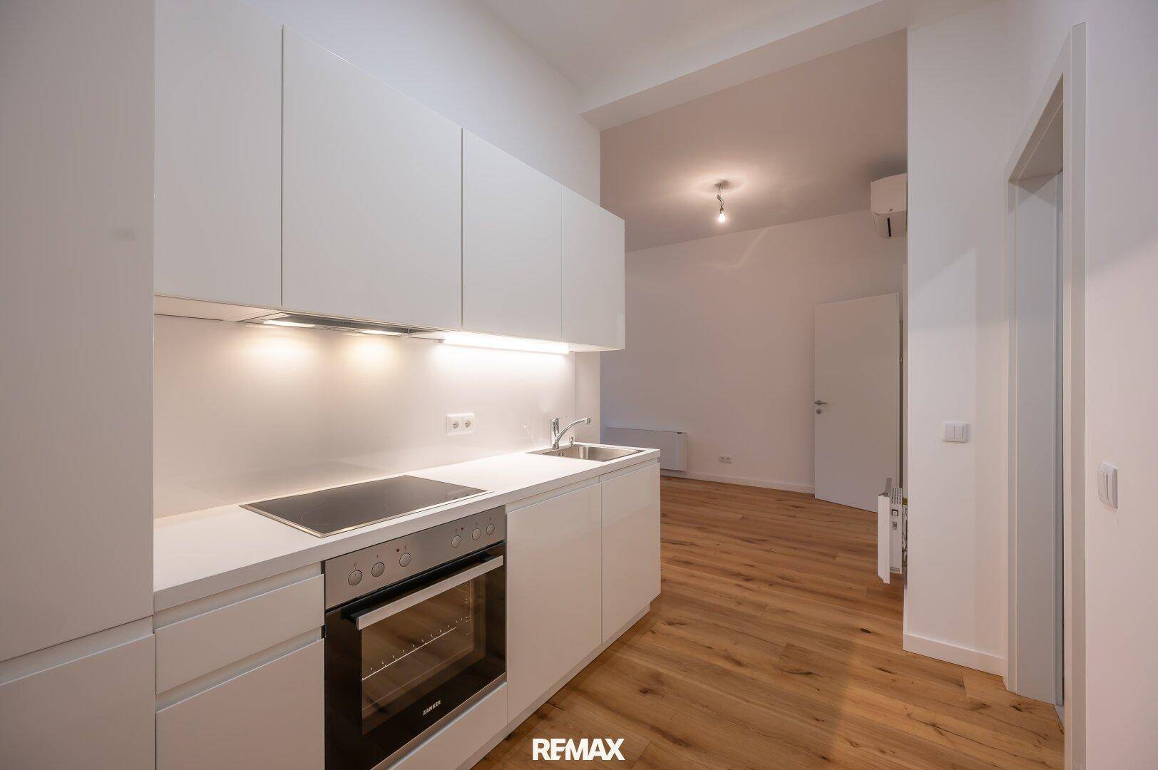 Moderne Einbauküche in Weiß mit Kochfeld, Backofen und viel Stauraum, kombiniert mit Holzboden.