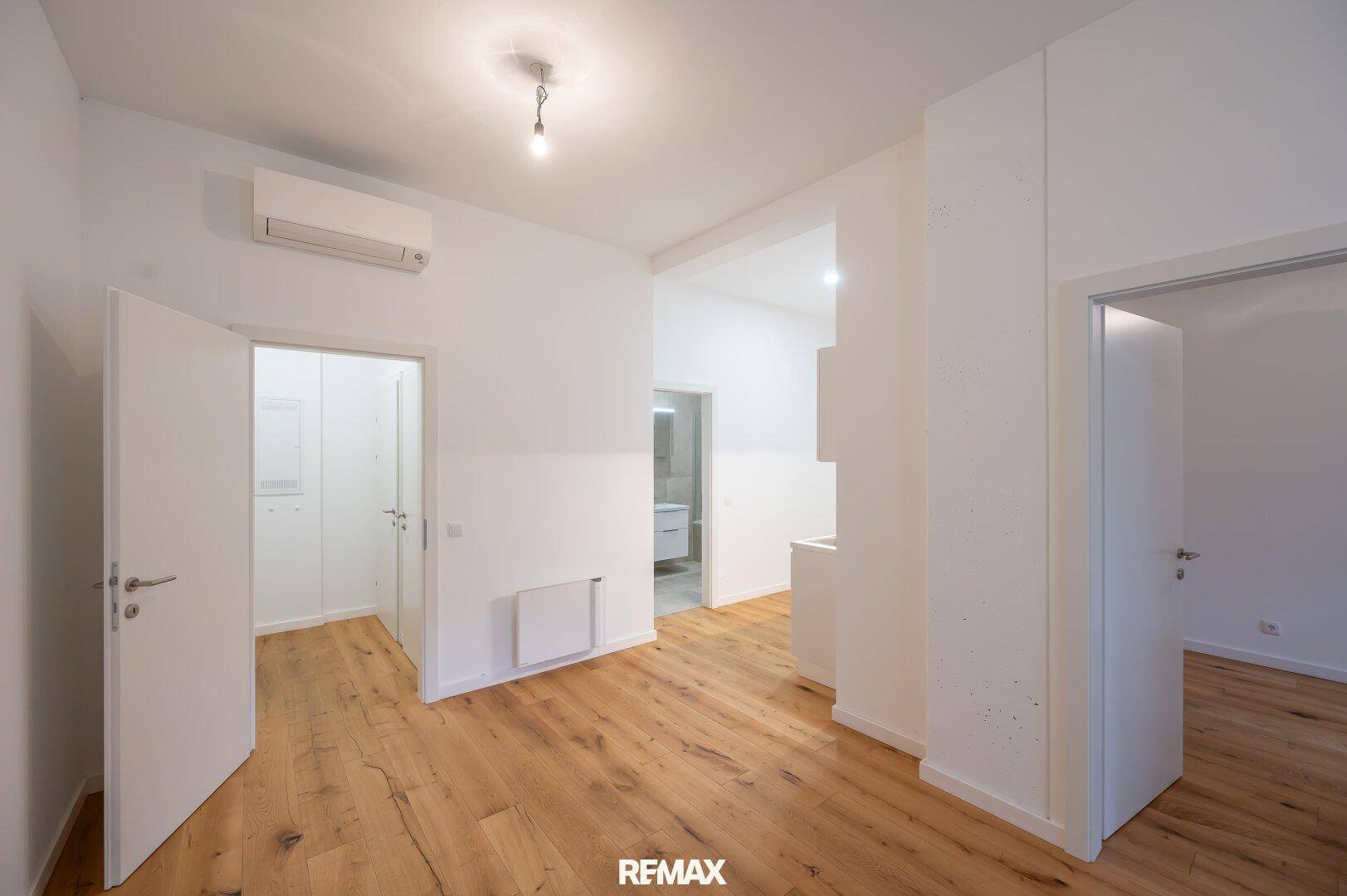 Heller Flurbereich mit Holzboden, weißen Wänden und Klimaanlage, verbindet mehrere Zimmer.