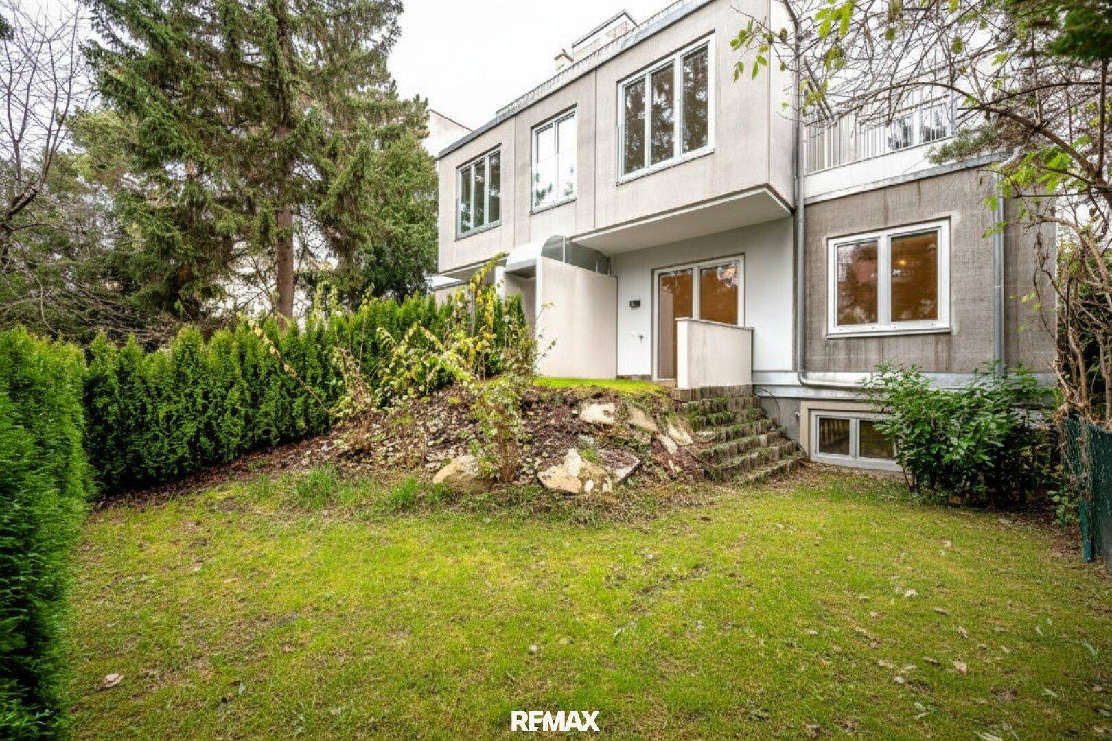 Moderne Gebäudefassade mit großen Fenstern, umgeben von einem gepflegten Garten mit Bäumen.