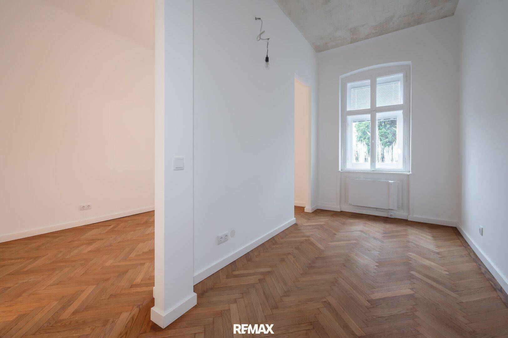 Geräumiger, heller Raum mit klassischem Fischgrätparkett und einem großen Fenster.
