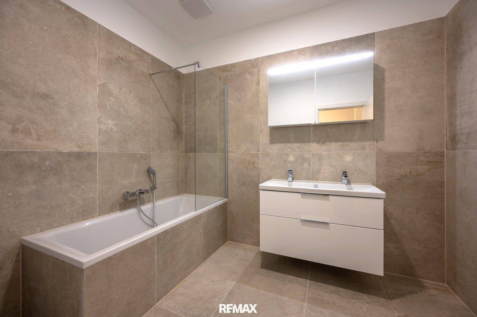 Modernes Badezimmer mit Badewanne, Doppelwaschbecken und großen Fliesen.