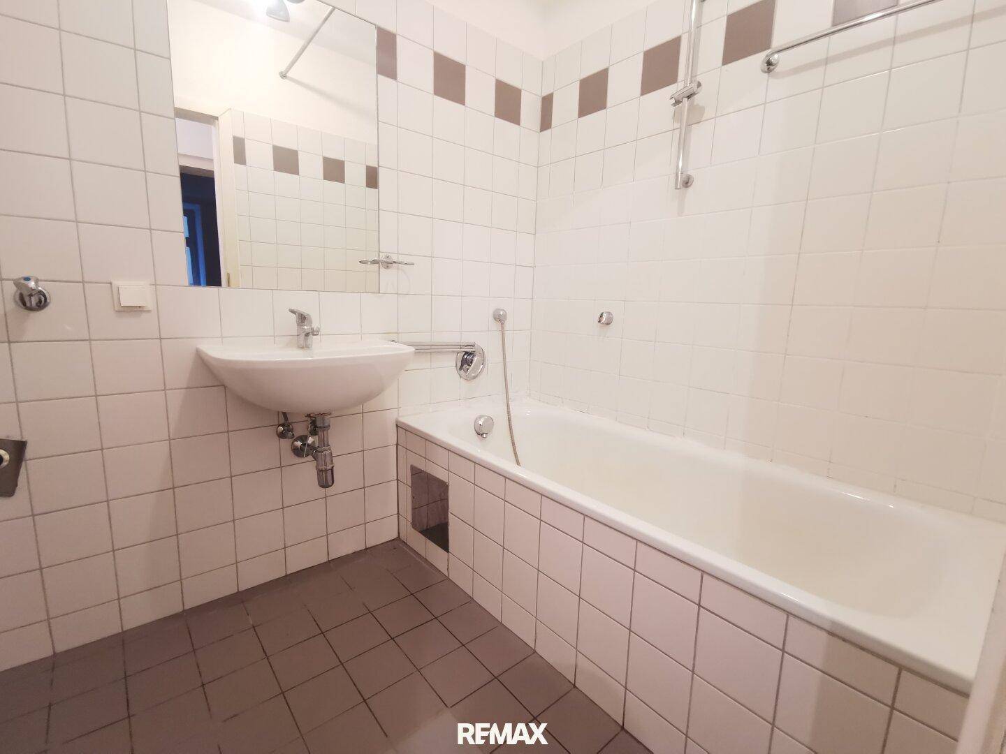 Gefliestes Badezimmer mit Badewanne, Waschbecken und Spiegel, in gutem Zustand.