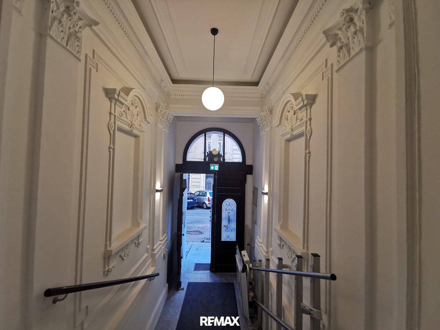 Eleganter Eingangsbereich mit Stuckverzierungen an Decke und Wänden sowie einer großen Eingangstür.