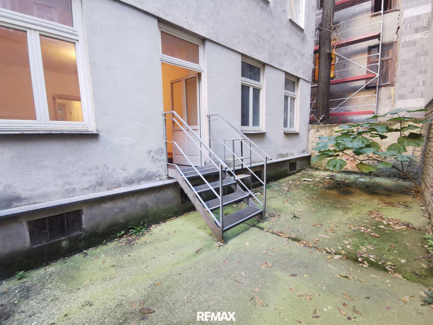 Hinterhofansicht eines Gebäudes mit Außentreppe und einem ungepflegten Gartenbereich.