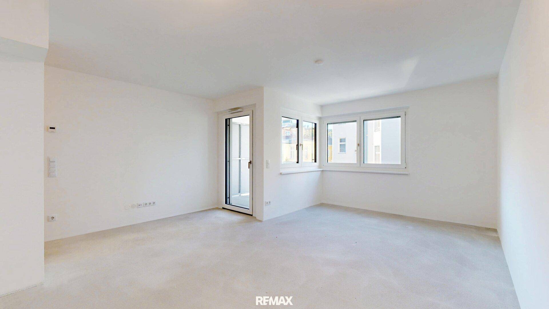 Heller, leerer Wohnraum mit großen Fenstern und Zugang zu einem Balkon.