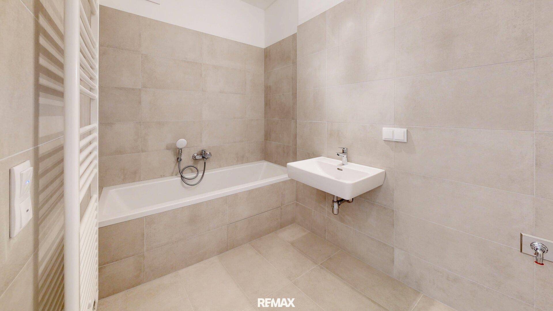 Modernes Badezimmer mit beigefarbenen Fliesen, Badewanne und Handtuchheizkörper.