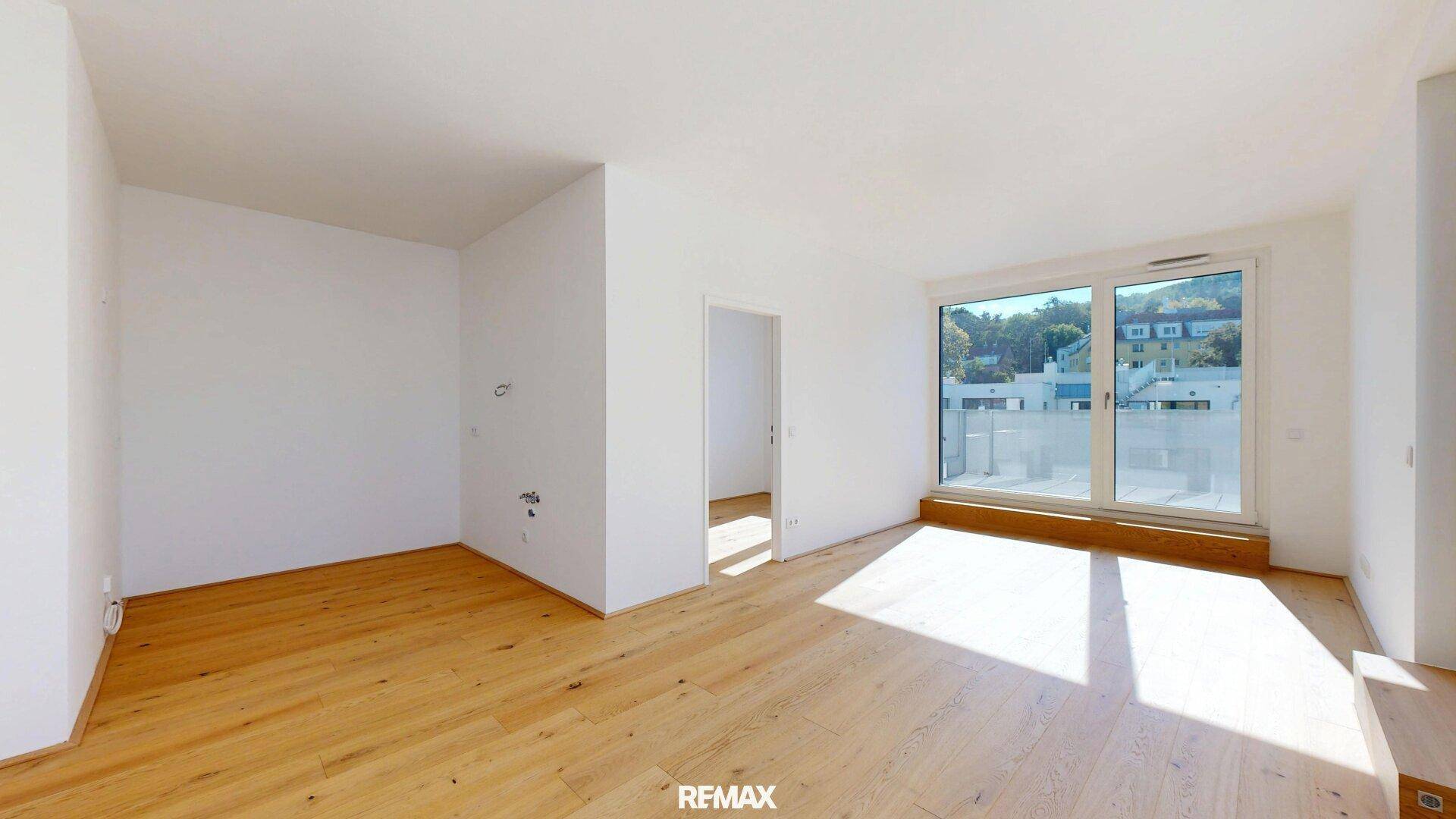 Heller, unmöblierter Raum mit Holzboden und großen Fenstern, die viel Tageslicht hereinlassen.
