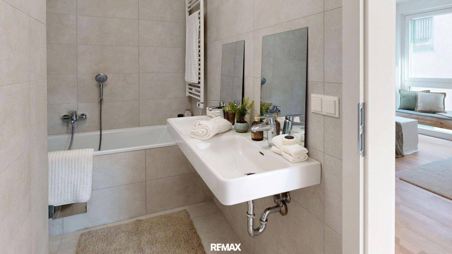Modernes Badezimmer mit hellgrauen Fliesen, Badewanne, wandmontiertem Waschbecken und Handtuchheizkörper.