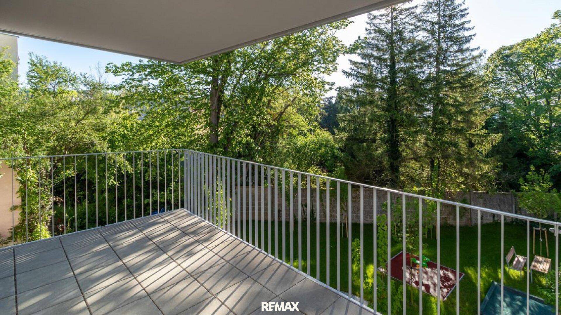 Geräumiger Balkon mit Fliesenboden und einem weiten Blick ins Grüne sowie auf einen Spielplatz.