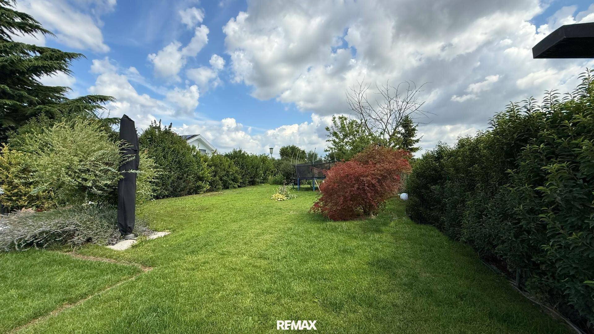 Weitläufiger Garten mit großer Rasenfläche, umgeben von Bäumen und Sträuchern.