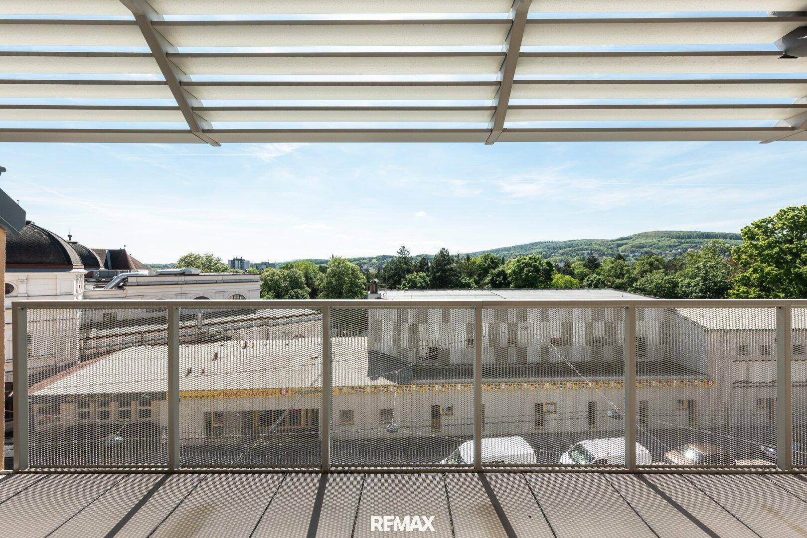 Moderner Balkon mit Überdachung und weitem Blick über die Stadt und grüne Hügel.