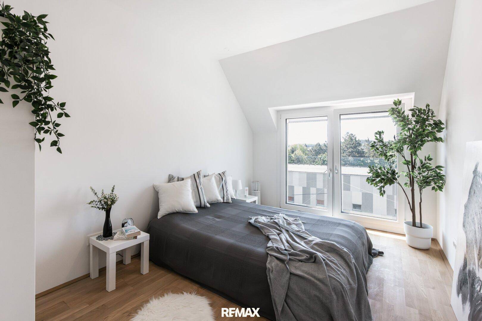 Schlafzimmer mit Dachschräge, großem Fenster und Zugang zu einem Balkon oder einer Terrasse.