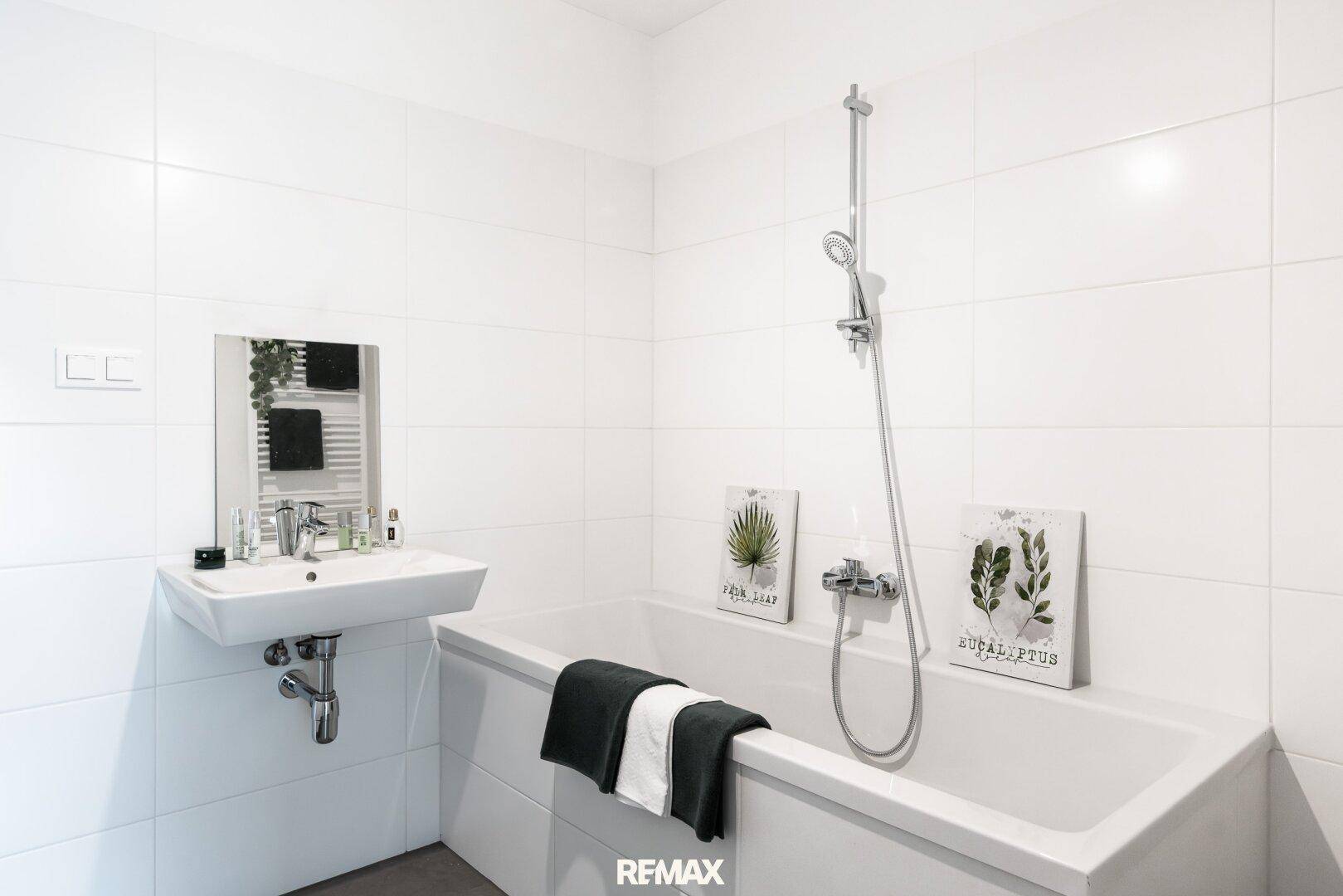 Modernes Badezimmer mit weißen Fliesen, Badewanne mit Duschfunktion, Waschbecken und Spiegel.