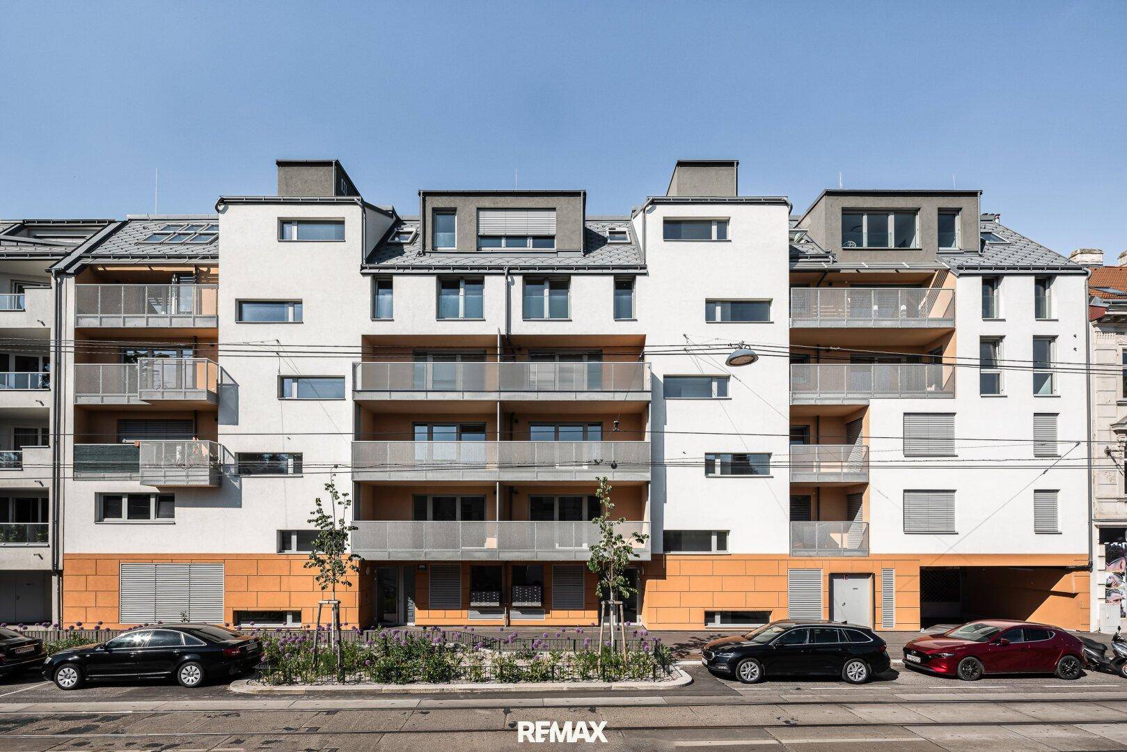 Moderne Wohnhausfassade mit weißen und orangefarbenen Akzenten sowie zahlreichen Balkonen.