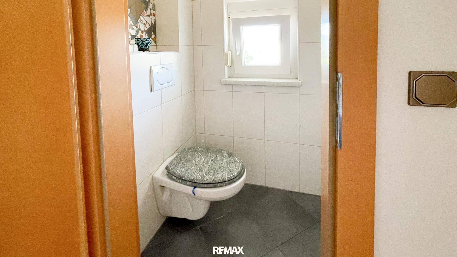 Kleines Gäste-WC mit dunklem Fliesenboden, wandhängendem WC und Fenster.