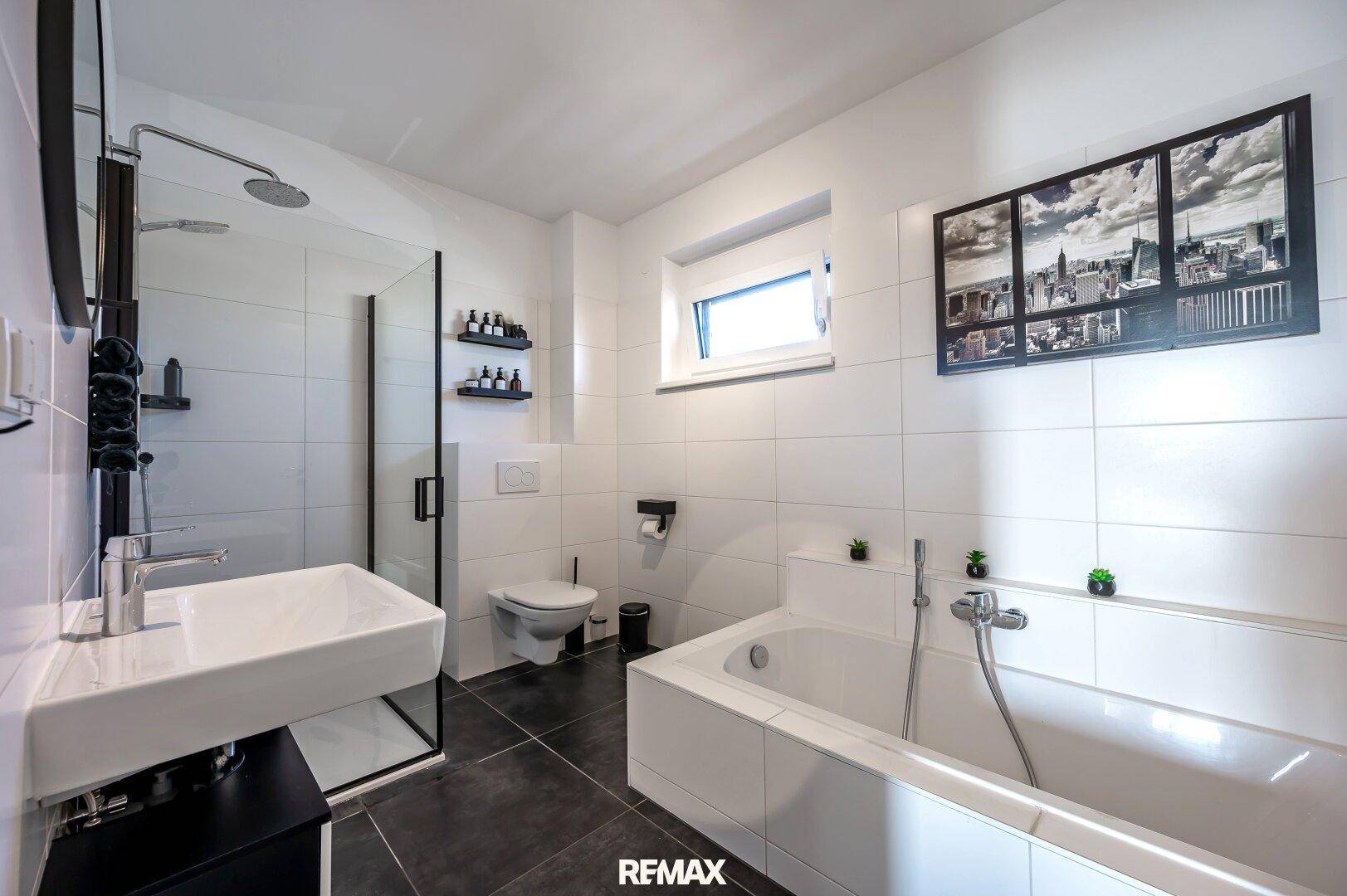 Modernes Badezimmer mit Badewanne, Dusche, WC und Fenster für Tageslicht.
