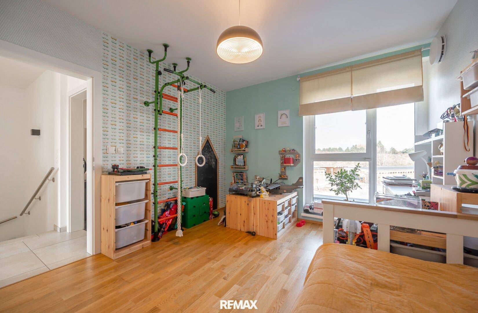 Kinderzimmer mit Holzboden, Spielgeräten und großem Fenster für viel Licht.