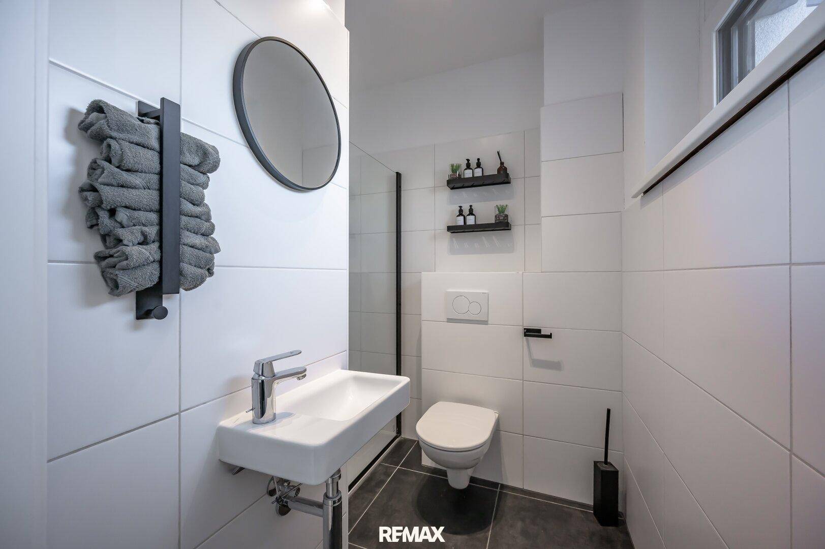 Modernes Gäste-WC mit Wand-WC, kleinem Waschbecken und Handtuchhalter.