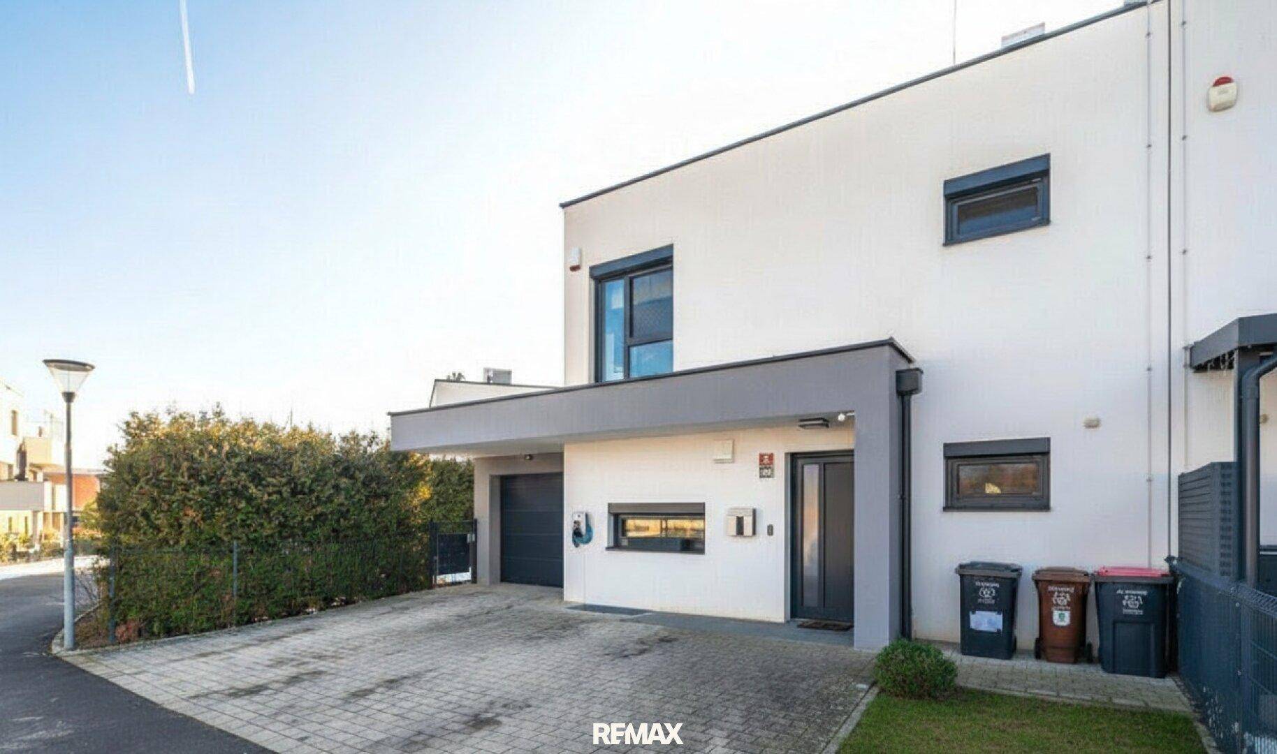 Moderne Doppelhaushälfte mit weißer Fassade, Carport und gepflasterter Einfahrt.