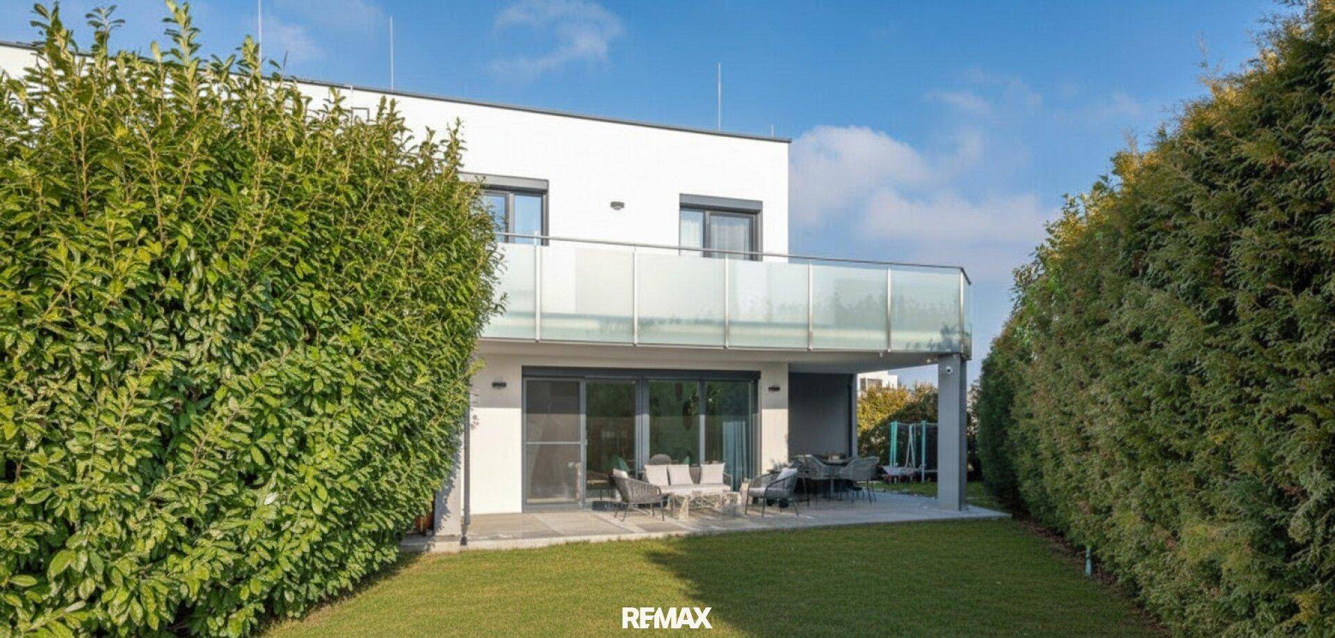 Hinterhof mit Rasenfläche, hoher Hecke und überdachter Terrasse mit Sitzgelegenheiten.