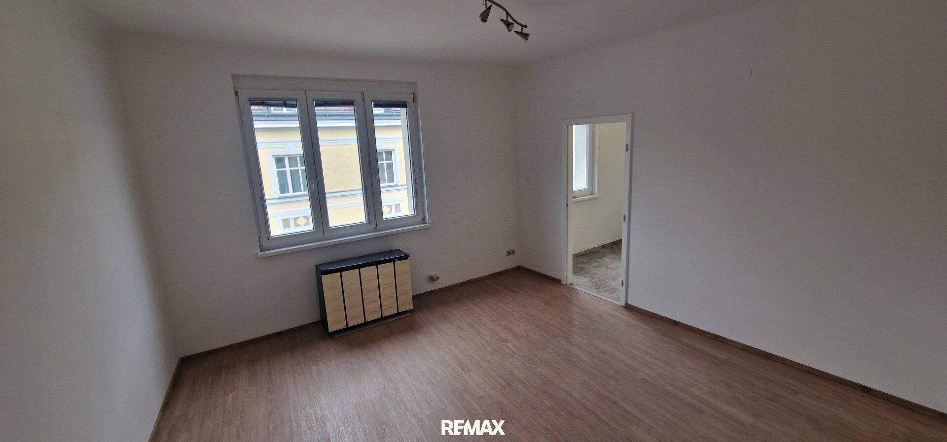 Leeres Wohnzimmer mit Holzboden und großen Fenstern, bereit zur individuellen Gestaltung.