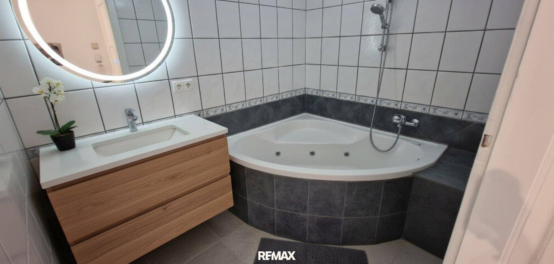 Modernisiertes Badezimmer mit Eckbadewanne und neuem Waschtisch mit beleuchtetem Spiegel.