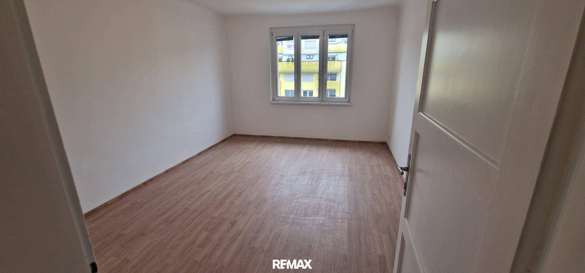 Leeres Schlafzimmer mit Holzboden und großen Fenstern, ideal für persönliche Einrichtung.
