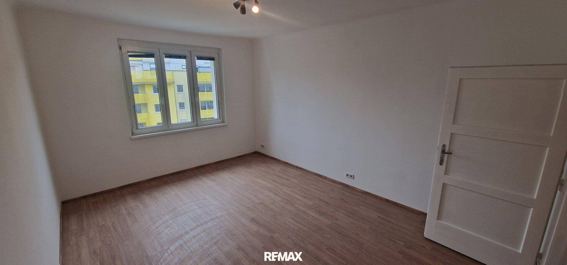 Weiteres leeres Schlafzimmer mit Holzboden und großen Fenstern, vielseitig nutzbar.