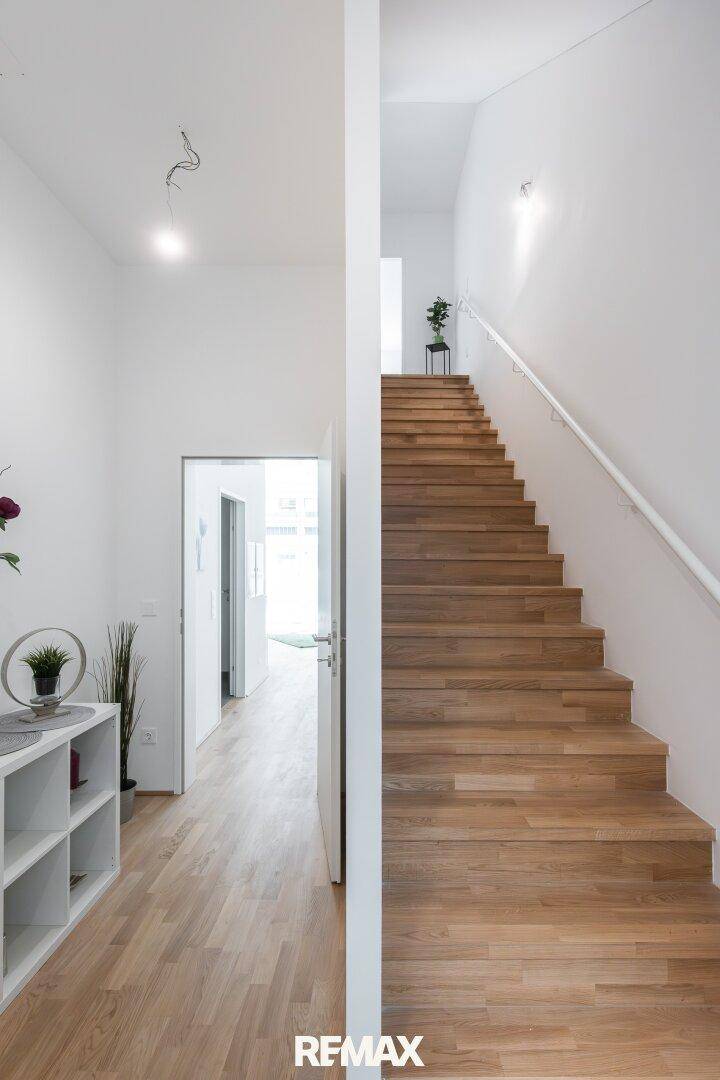 Heller Flur mit Holztreppe und Zugang zu weiteren Räumen, modern und funktional gestaltet.