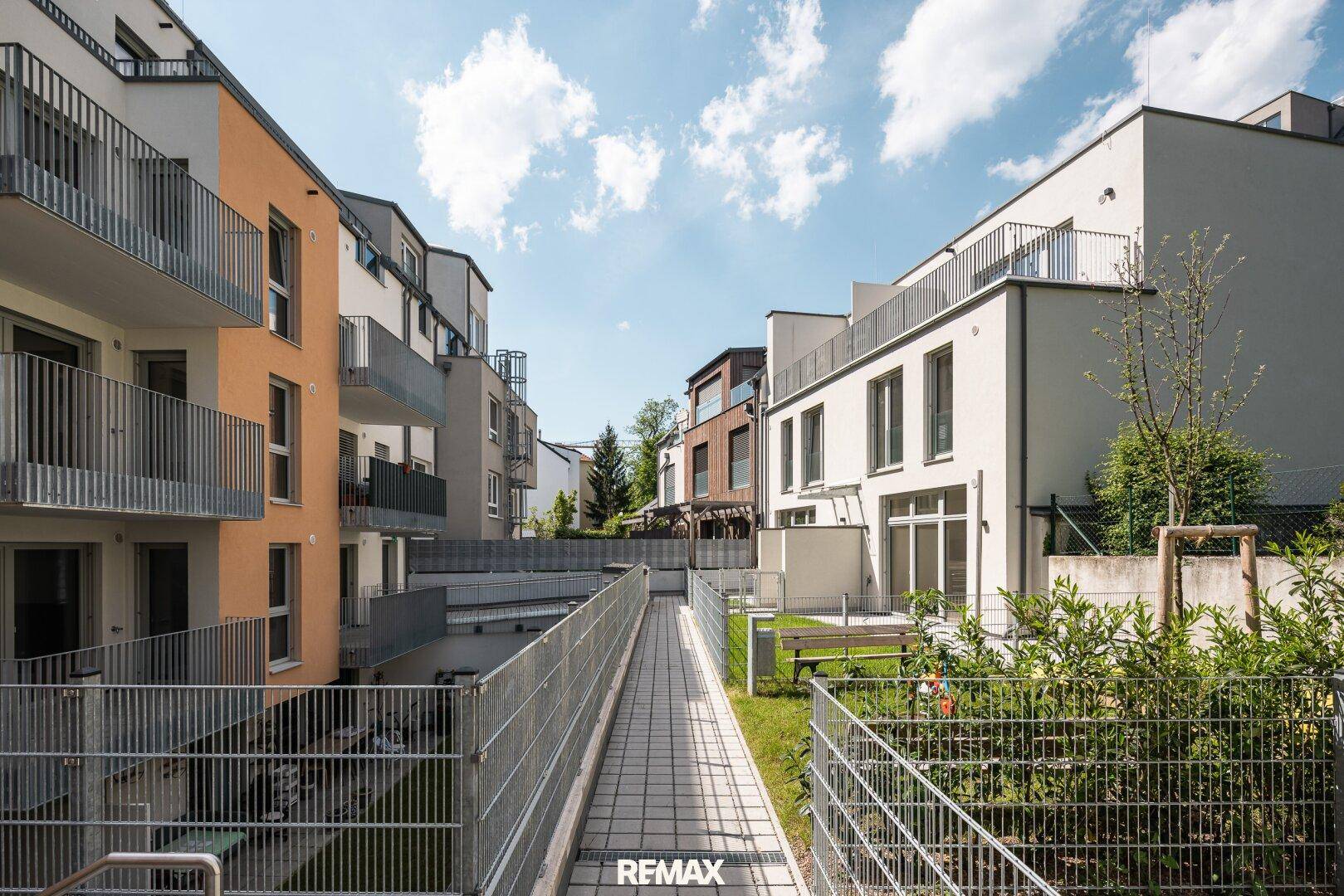 Moderne Wohnanlage mit mehreren Gebäuden, Balkonen und einer barrierefreien Rampe im Außenbereich.