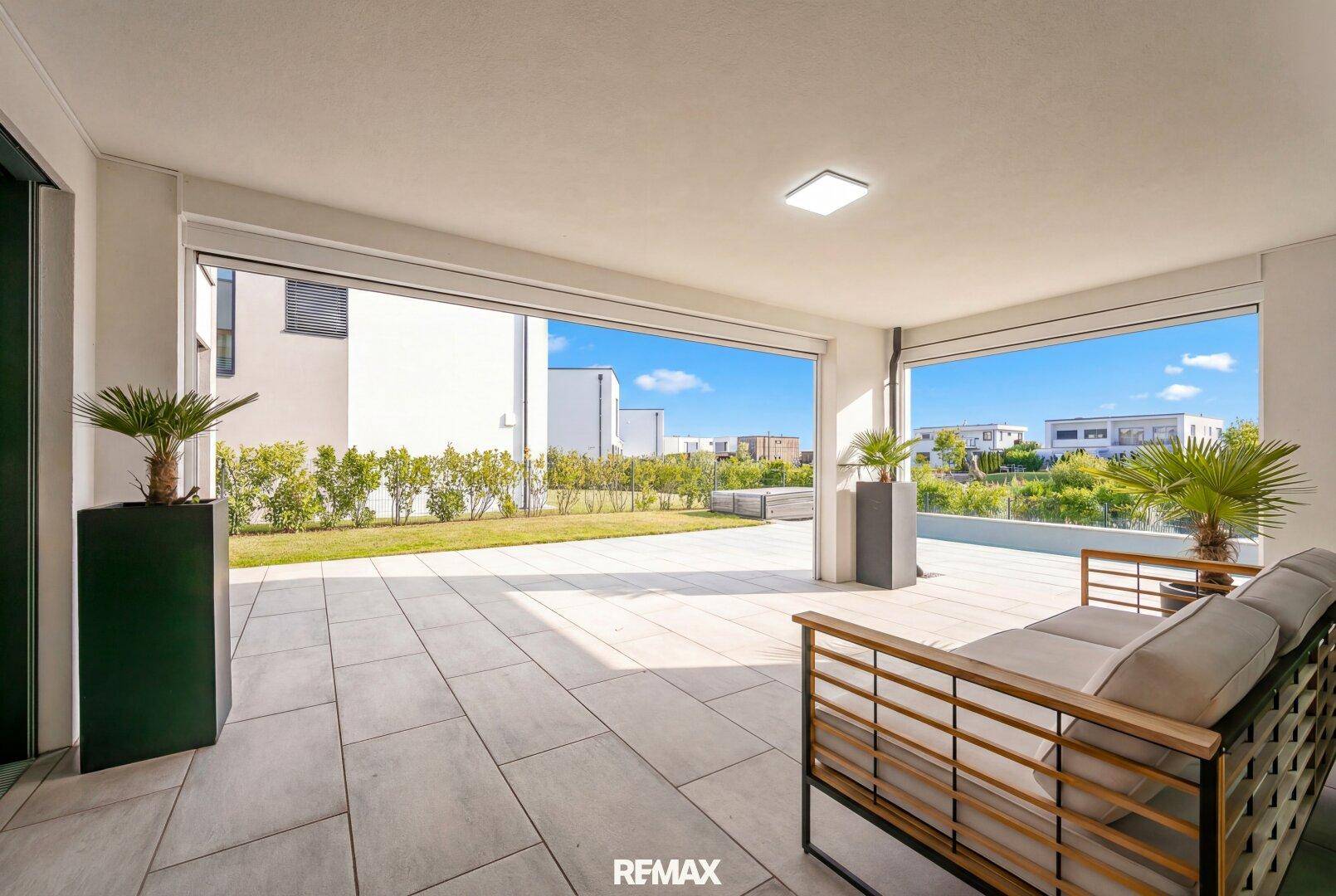 Großzügige überdachte Terrasse mit Sitzgelegenheiten und direktem Zugang zum grünen Garten.