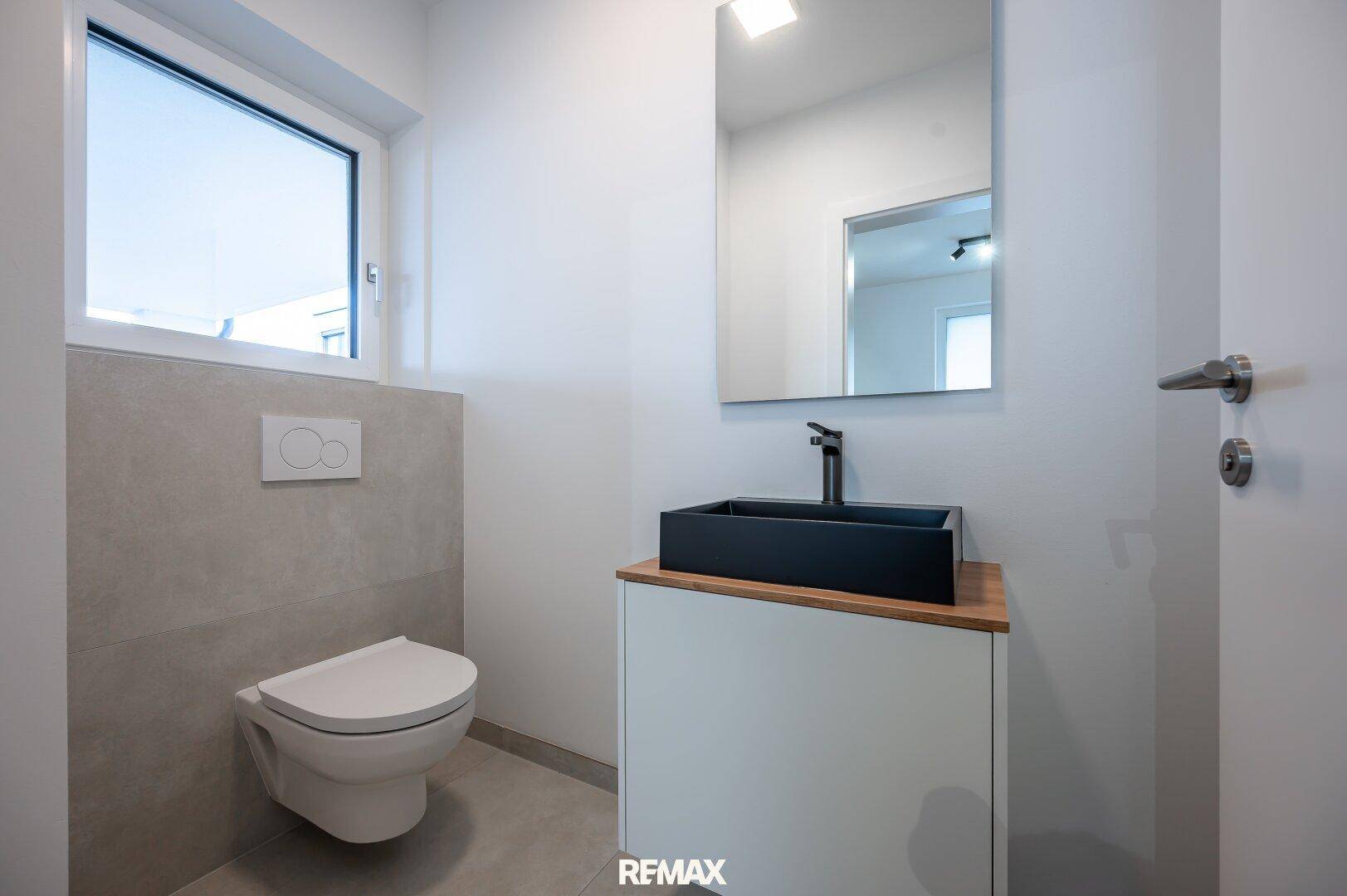 Modernes Gäste-WC mit wandhängendem WC, stilvollem Waschbecken und Fenster für Tageslicht.