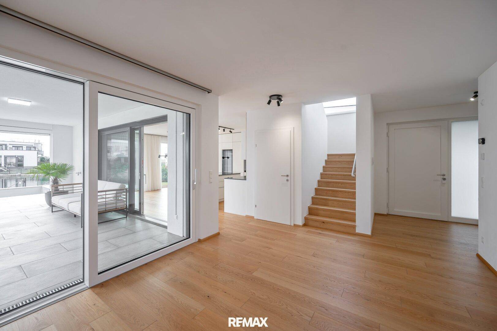 Offener Wohnbereich mit Holzboden, Zugang zur Küche und einer eleganten Holztreppe.