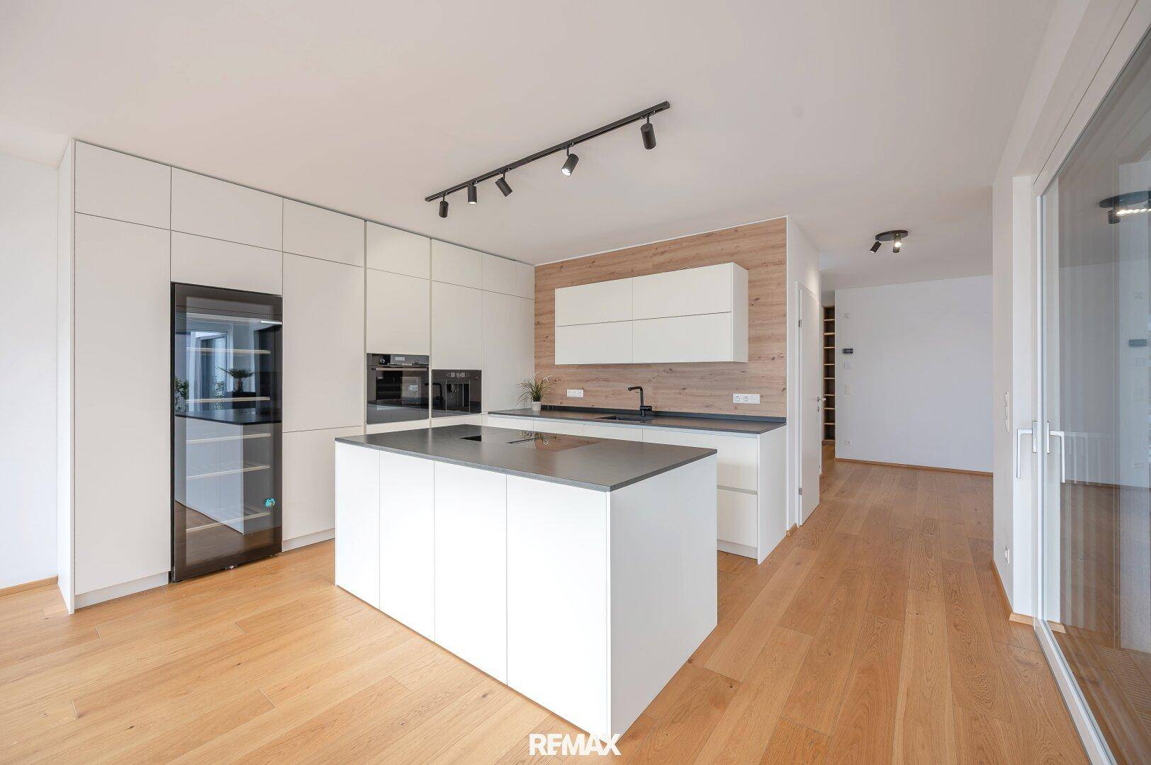 Moderne Einbauküche mit weißen Fronten, Kücheninsel, integrierten Geräten und Holzboden.