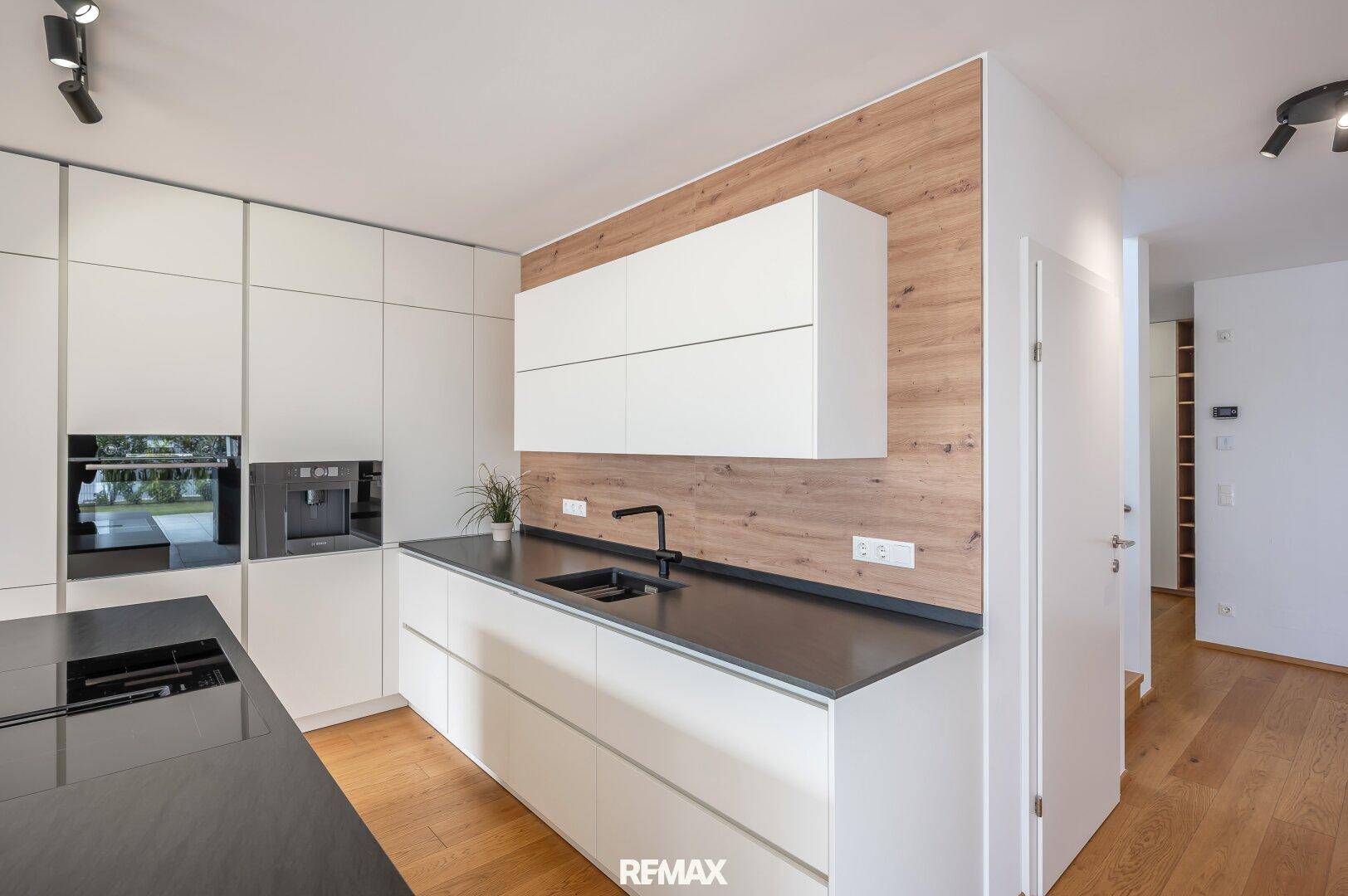 Elegante Küche mit weißen Schränken, dunkler Arbeitsplatte und einer stilvollen Holzwandverkleidung.
