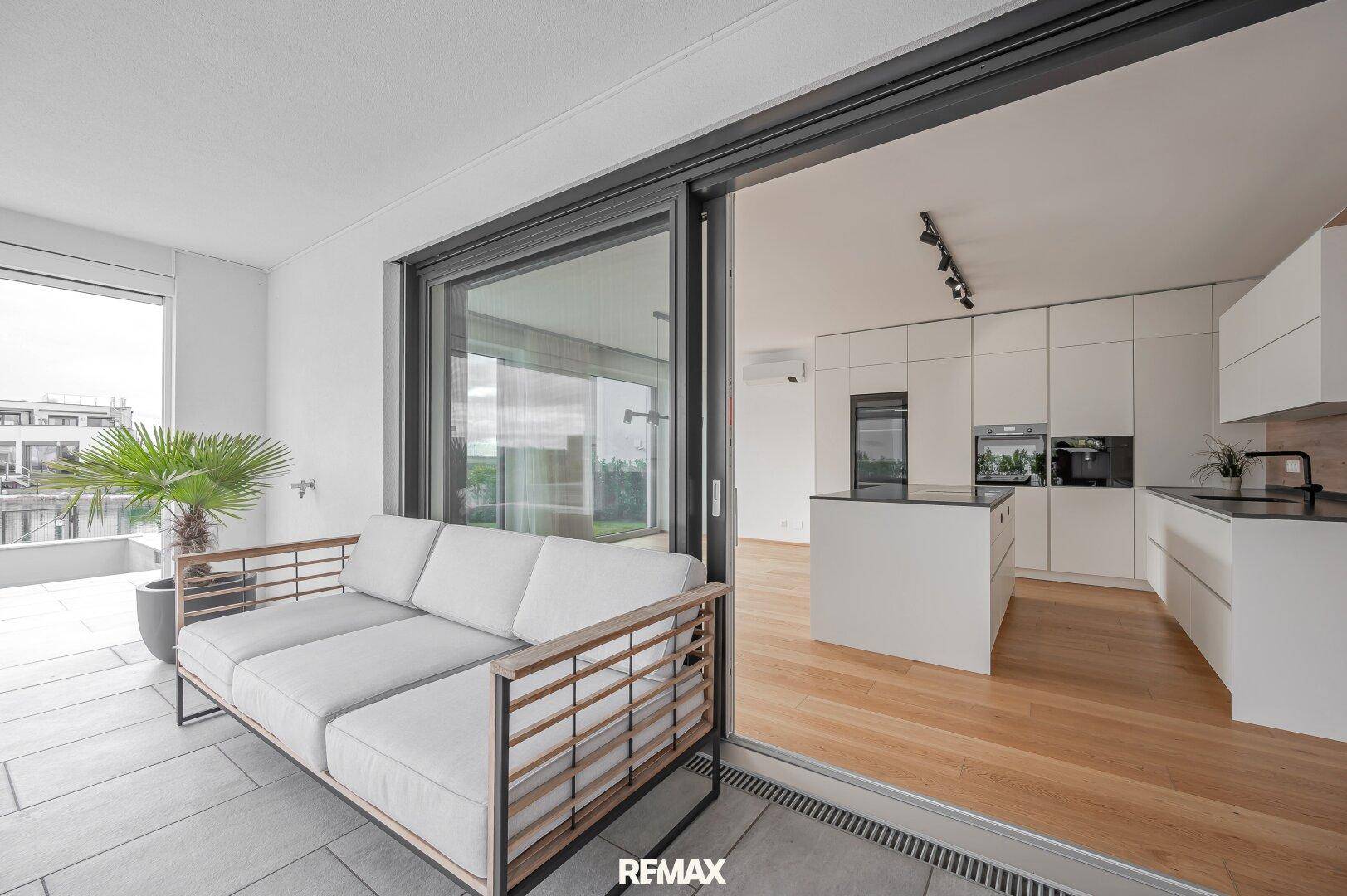 Überdachte Loggia mit Sofa und direktem Zugang zur modernen Küche durch große Schiebetüren.