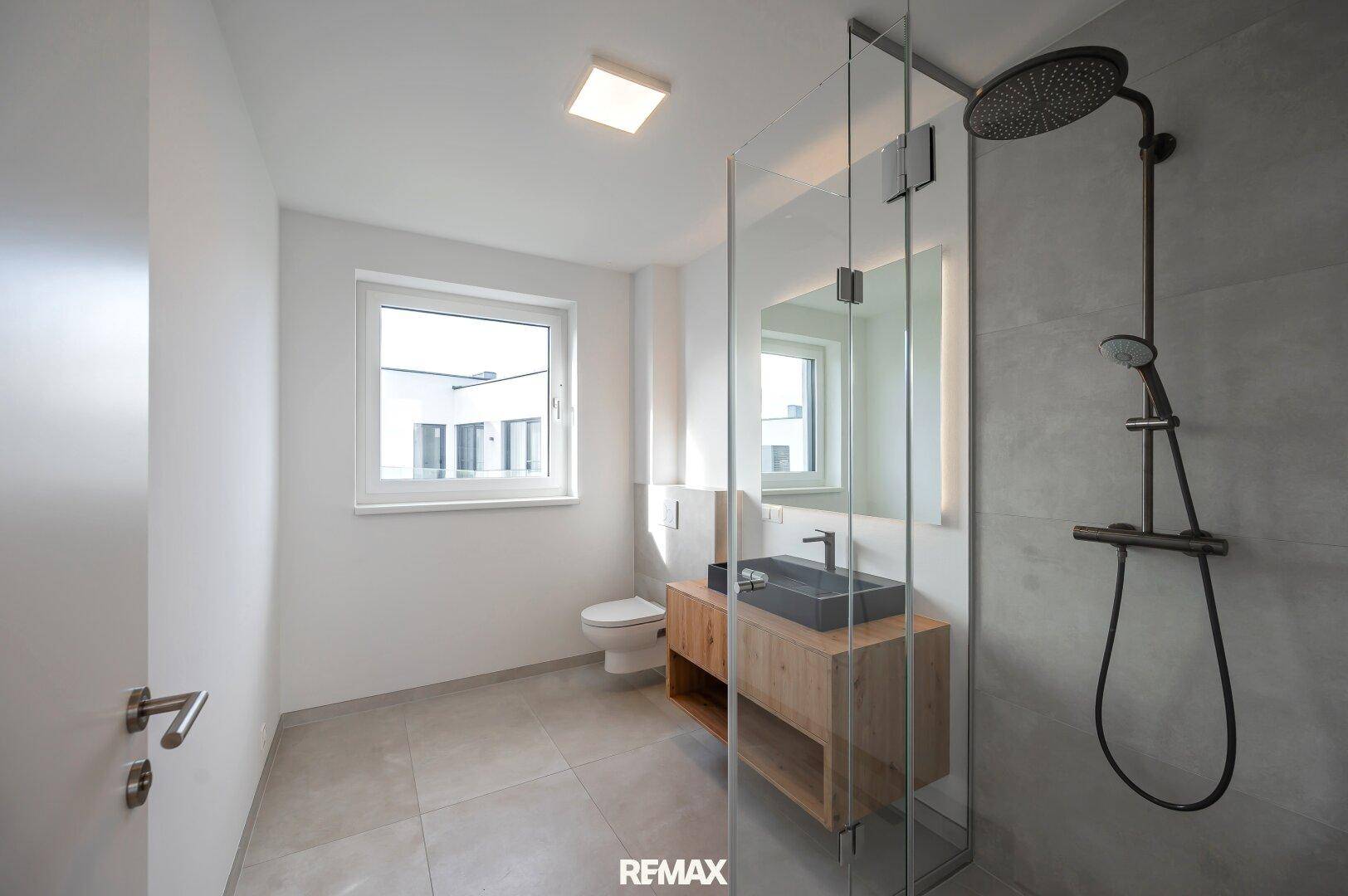 Modernes Badezimmer mit ebenerdiger Dusche, WC, Einzelwaschbecken und Fenster für Tageslicht.