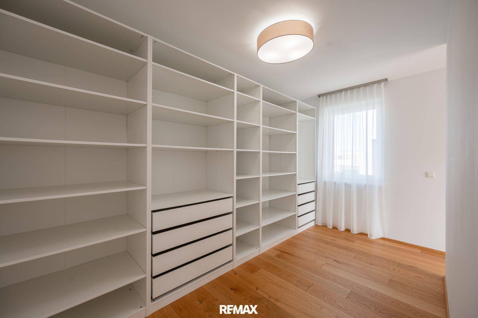 Geräumiger begehbarer Kleiderschrank mit vielen Regalen, Schubladen und Fenster.