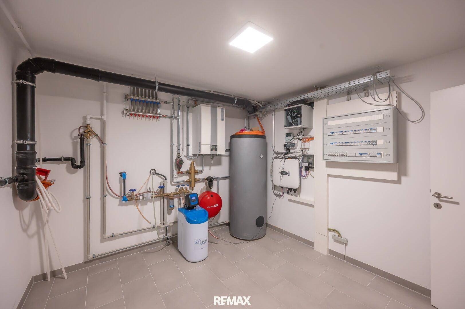 Technikraum mit Warmwasserspeicher, Heizungsverteilern und elektrischen Schaltkästen.