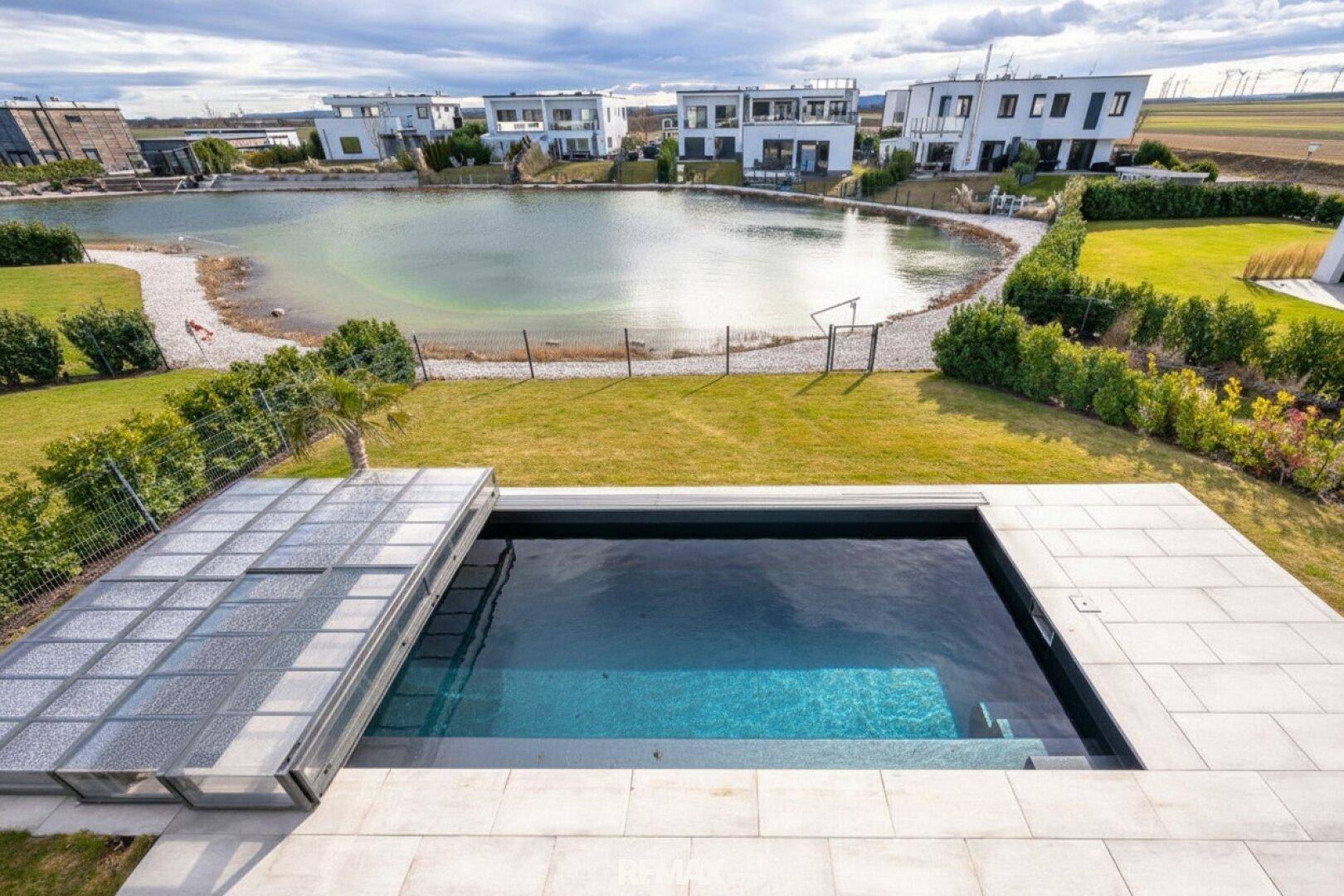Außenbereich mit privatem Pool, Rasenfläche und Blick auf einen Naturteich sowie moderne Häuser.