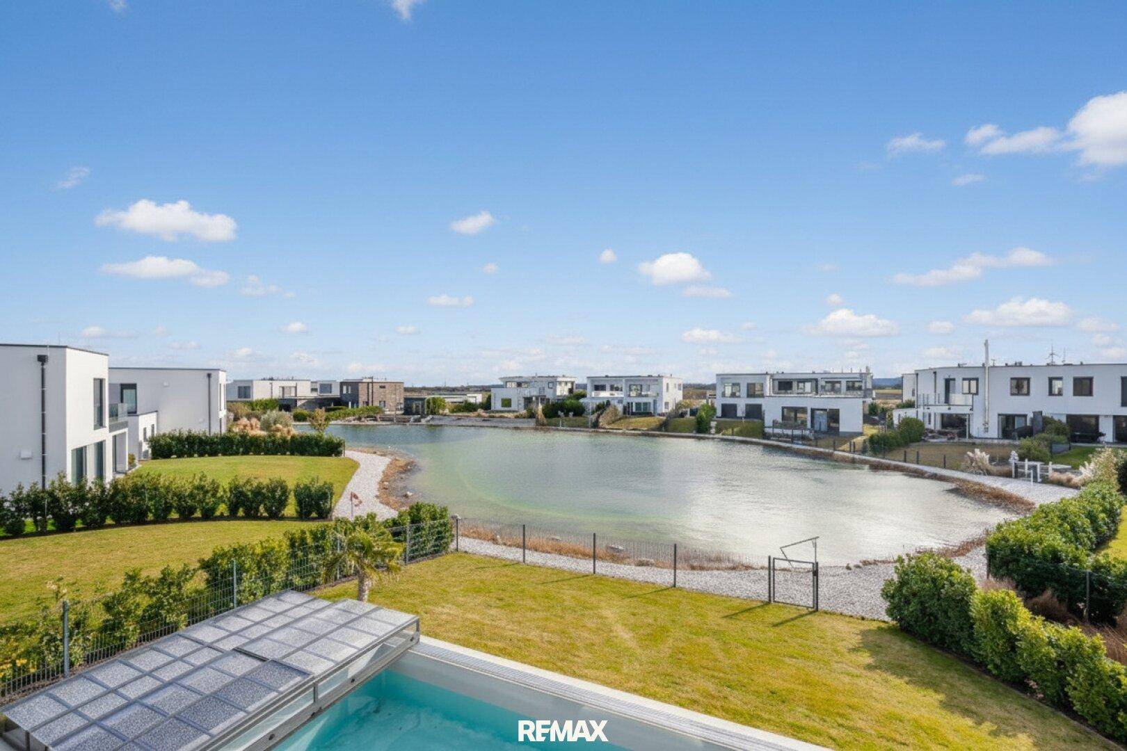 Weitläufiger Blick auf den See und die moderne Wohnsiedlung unter blauem Himmel.