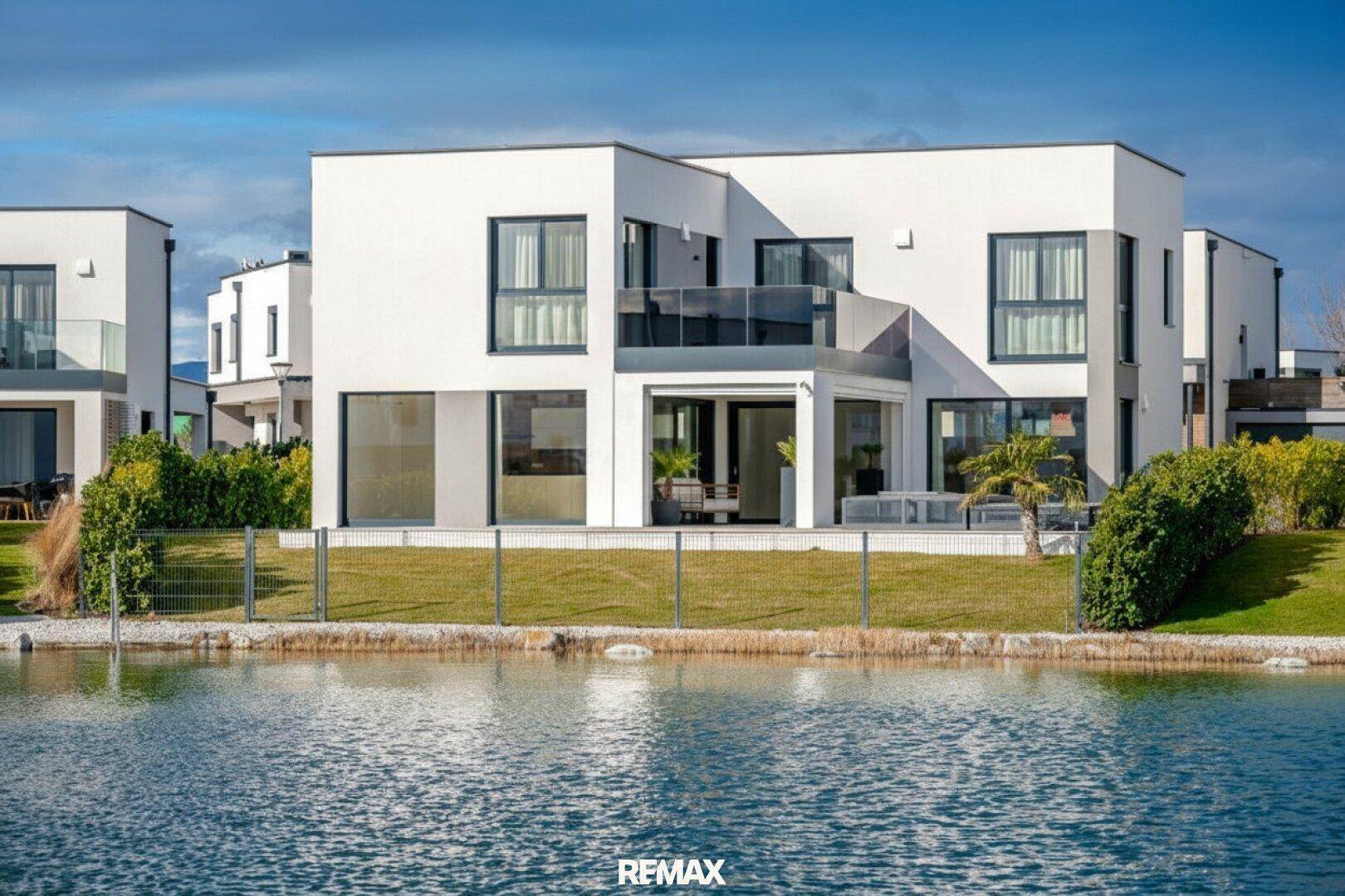 Moderne weiße Villa mit großen Fenstern, Balkon und Blick auf das Wasser.