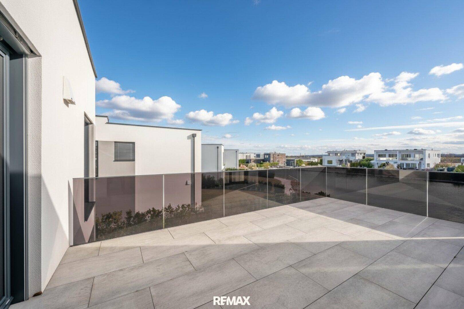 Große, geflieste Terrasse mit Glasgeländer und weitem Blick auf die Umgebung.