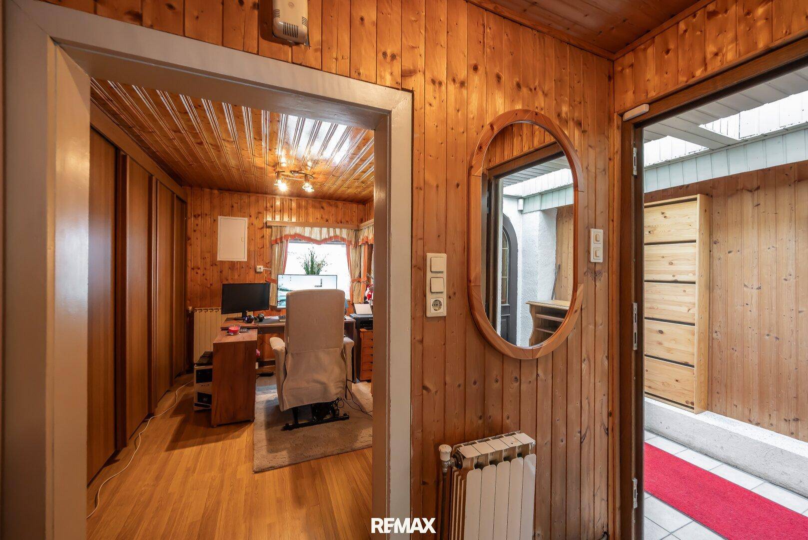Gemütlicher Flur mit Holzverkleidung und Blick in ein helles Arbeitszimmer mit Schreibtisch und Bürostuhl.