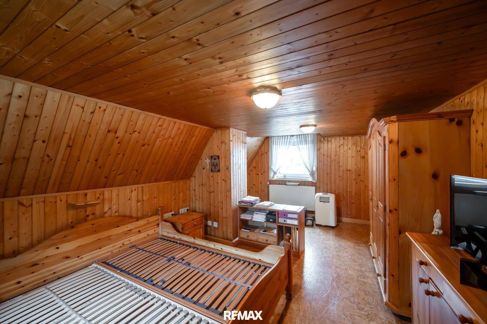 Schlafzimmer mit rustikaler Holzverkleidung an Wänden und Decke, sowie einem Holzbettrahmen und Fenster.