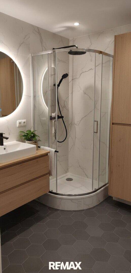 Modernes Badezimmer mit begehbarer Dusche, runden Spiegeln und Holzwaschtisch, hochwertig ausgestattet.