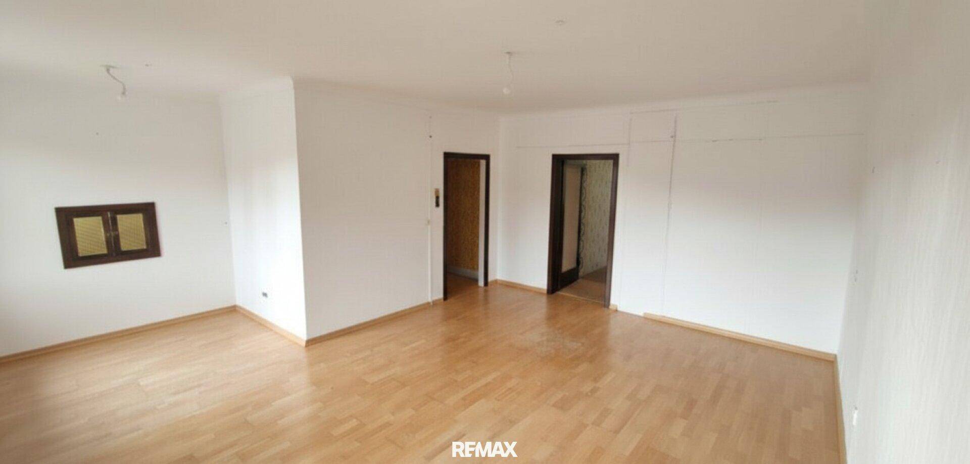 Leeres Wohnzimmer mit Holzboden und weißen Wänden, bereit zur individuellen Gestaltung und Einrichtung.